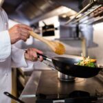 Chef sauteing vegetables in a black pan with a wooden spoon 1400